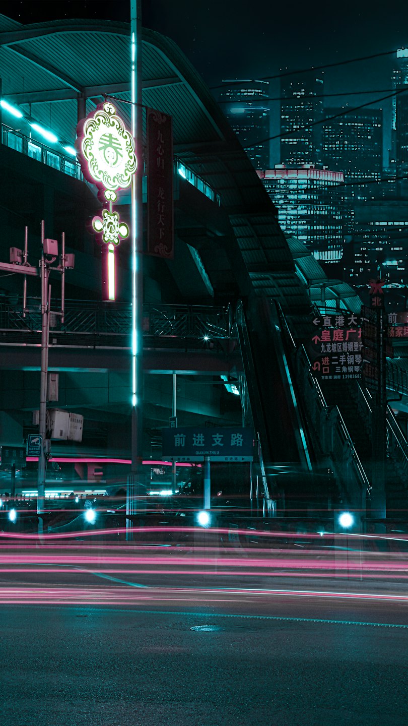 Neon signs and light trails illuminate a busy city street.