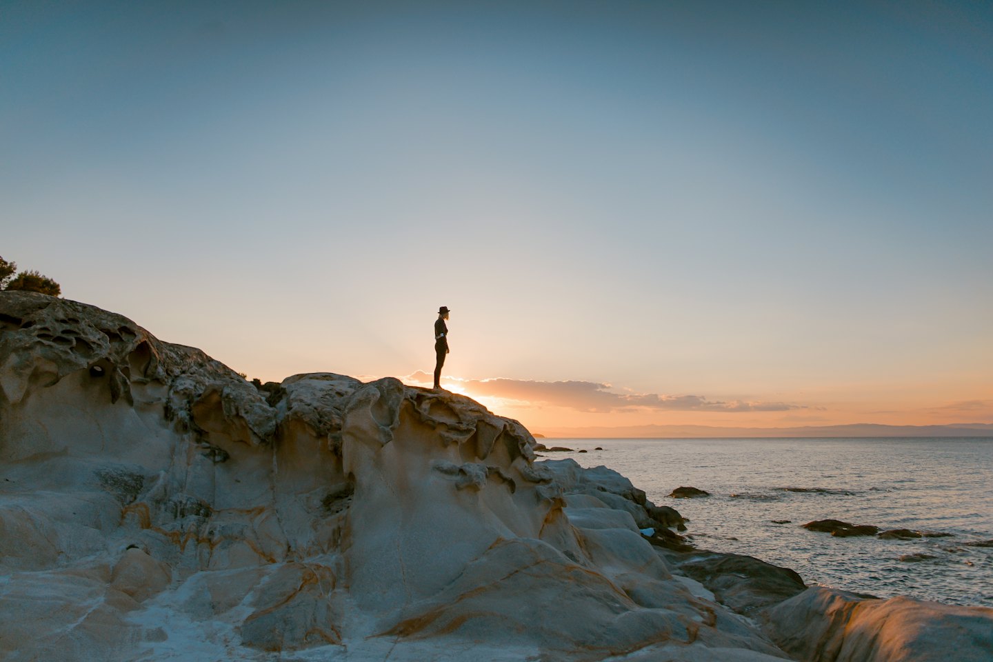 A person stands on a cliff edge looking over the sea.